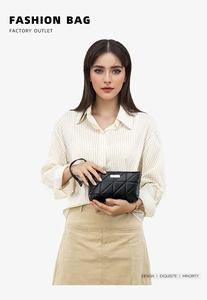 Close-up of a black quilted clutch bag featuring a silver metal logo and wrist strap
