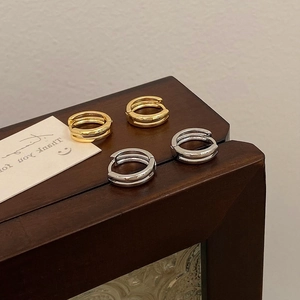 Minimalist double-layered gold and silver hoop earrings displayed on a wood box