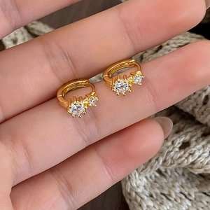 Detailed view of hand-held gold huggie earrings with sparkling double round zircons