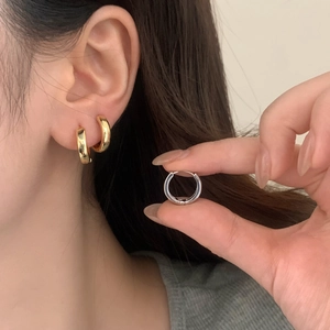 Close-up of minimalist gold and silver hoop earrings worn on ear with high-polish finish