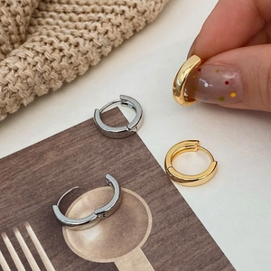 Polished gold and silver hoop earrings displayed on a warm knitted texture background