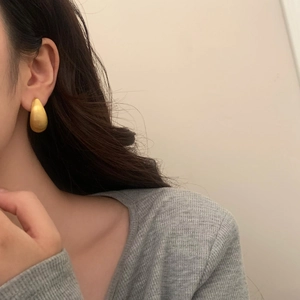 Boucles d'oreilles goutte en or mat avec finition en métal brossé portées par un mannequin