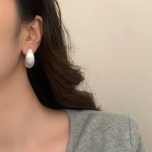 Gros plan de boucles d'oreilles goutte en argent mat montrant la texture du métal sur le mannequin