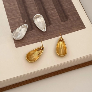 Détail de boucles d'oreilles goutte dorées et argentées avec finition métal brossé