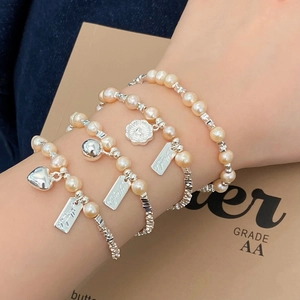 Detail eines vierteiligen Perlenarmband-Sets mit silbernen Herzanhängern und Gravurplatten