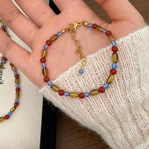 Detail of red agate and amber beaded necklace with gold lobster clasp on white sweater