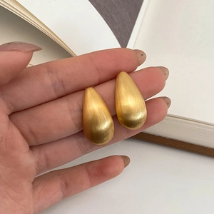 Gros plan sur des boucles d'oreilles goutte dorées avec finition en métal brossé