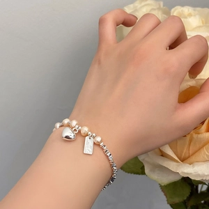 Elegantes Süßwasserperlenarmband mit Herzanhänger und graviertem Tag an dem Handgelenk
