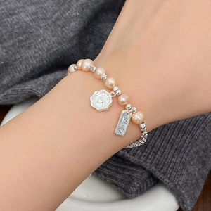 Detail eines rosa Perlenarmbands mit Herzanhänger aus Silber und Gravur am Handgelenk