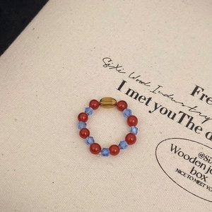 Detail of beaded ring with red agate, blue crystals and golden oval beads on textured board