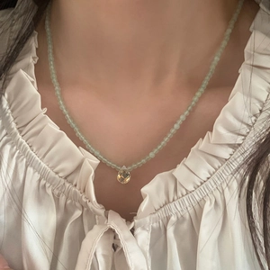 Detail view of light green beaded necklace with yellow faceted teardrop pendant on model