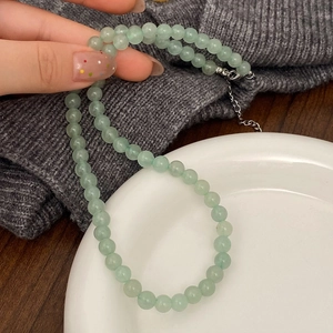 Natural light green stone beaded necklace with silver chain shown on hand and a ceramic plate