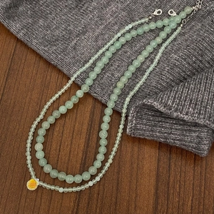 Detail view of double-layer light green stone necklace with teardrop crystal pendant