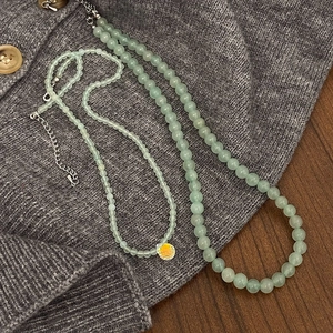 Detail of green stone bead necklaces with a yellow heart pendant on a soft knit fabric