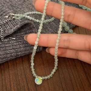Detail of light green beaded necklace with faceted iridescent crystal pendant on metal chain