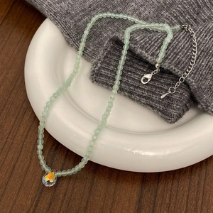 Detail of beaded necklace with light green natural stones and aurora teardrop pendant