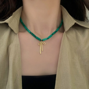 Detail of green malachite bead necklace with a golden bow pendant on a model