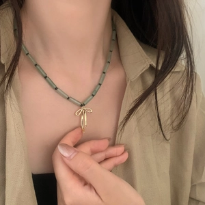 Detail of green stone bead necklace with a golden bow pendant on a model neckline