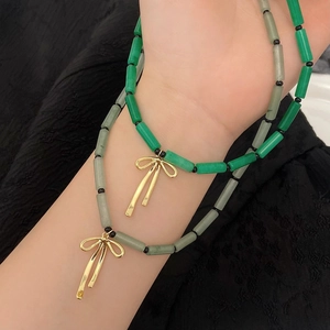 Close-up of green bamboo-style natural stone necklace with gold bow pendant on model