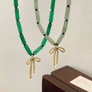 Detail of green bamboo stone beaded necklaces with gold bow pendants on a gift card