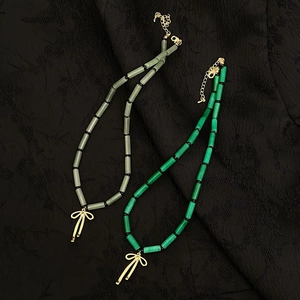 Detail of green stone bead necklaces with elegant gold bow pendants on black fabric