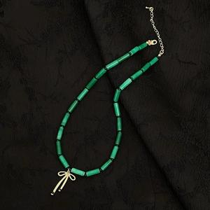 Macro view of green bamboo-shaped natural stone beads and golden bow pendant necklace