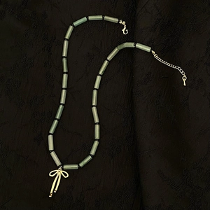 Detail of green stone bead necklace with a gold bow pendant on a black fabric background