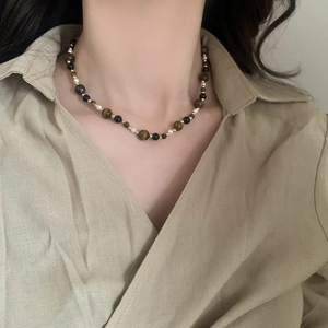 Detail of beaded necklace with tiger eye stones and pearls on a linen shirt