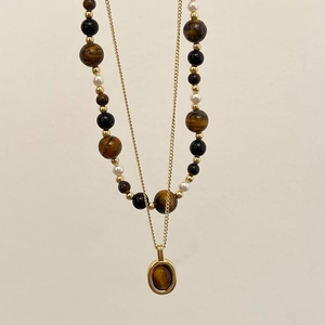 Detail of double-layer beaded necklace featuring tiger eye stones and a gold pendant