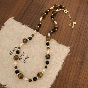 Close-up of beaded necklace with tiger eye stones and pearls on vintage paper