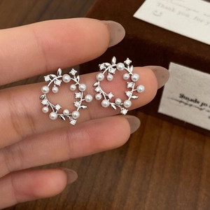 Detail of silver wreath earrings with white pearls and crystals held over a gift box