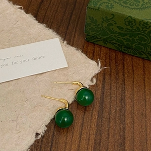 Macro detail of green chalcedony stud earrings with gold finish on vintage paper