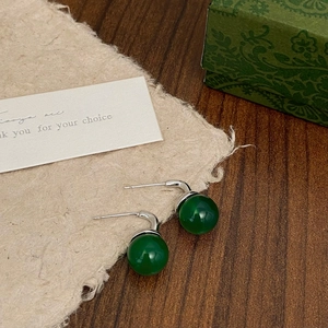 Macro detail of retro green chalcedony earrings with silver hooks on vintage paper