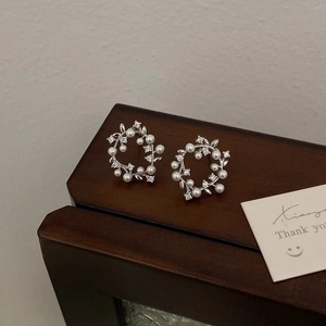 Detail of silver vine earrings with white pearls and sparkling zircons on wood