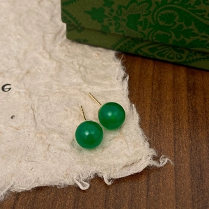 Macro detail of round green chalcedony stud earrings with gold pins on retro paper