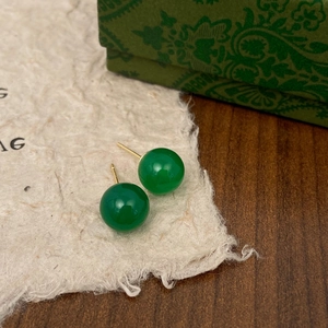 Detailed view of green chalcedony stud earrings with gold plating on textured paper