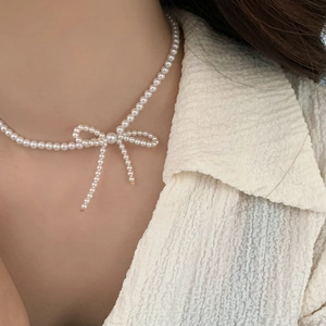 Close-up of elegant pearl necklace with handcrafted bow pendant and tassels on neck