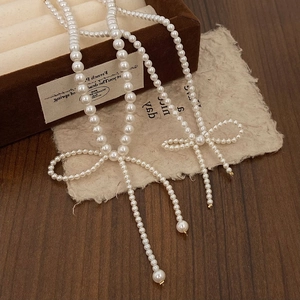 Elegant pearl necklace featuring a woven bow and long tassels on a velvet jewelry box