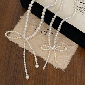 Detail of elegant white pearl necklaces with woven pearl bow pendants on wood background