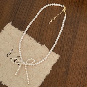 Elegant pearl necklace detail with a bow pendant and gold clasp on a vintage wood surface