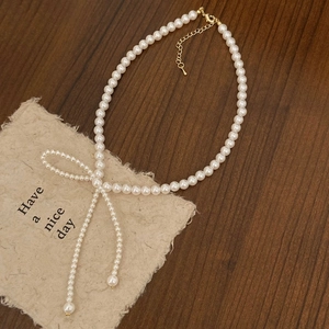 Detail of white pearl necklace featuring a pearl-studded bow and gold lobster clasp