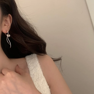 On-ear view of minimalist silver bow tassel earrings with a sleek knotted design