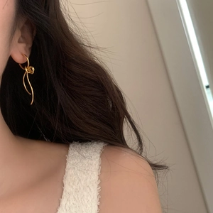 Detail of golden metal bowknot earrings with wavy tassels on a female model