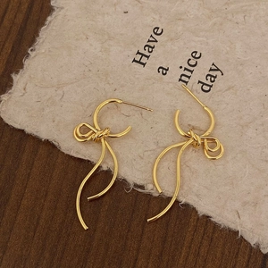 Close-up of golden bow-shaped drop earrings with fluid metal tassels on vintage paper