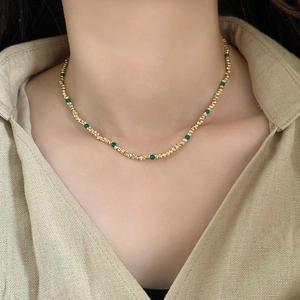 Collier élégant en perles dorées avec pierres vert émeraude sur un mannequin chic