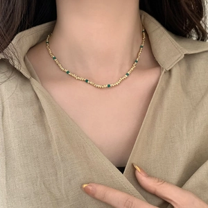 Détail d'un collier de perles dorées élégant avec pierres vertes sur une chemise kaki