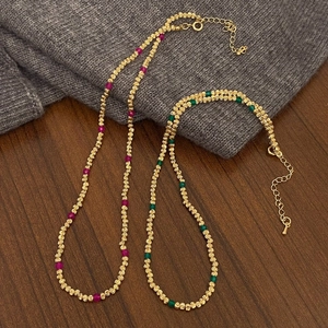 Colliers en perles dorées avec pierres précieuses roses et vertes sur un tissu texturé