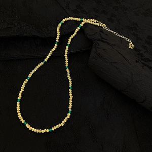 Détail d'un collier de perles plaqué or avec pierres vertes sur soie noire