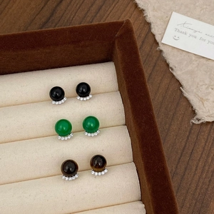 Detailed view of three pairs of stud earrings with green, black, and brown stones in a box