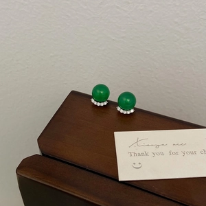 Detailed shot of green chalcedony earrings with micro-set zircon on dark wood surface